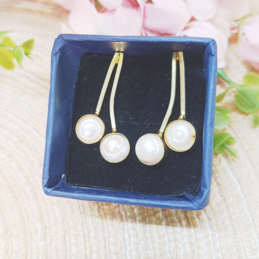Close-up of gold curved earrings with two pearls – handcrafted minimalist jewelry by Gemsara.