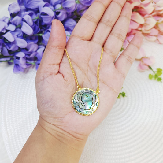 Close-up of Abalone pendant necklace in hand – round shell design with iridescent green and blue tones.