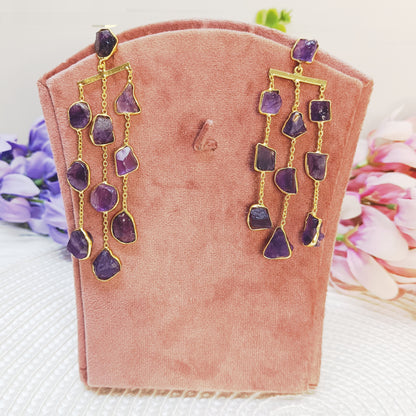 Raw amethyst waterfall earrings in gold plating displayed on pink velvet stand 
