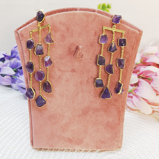 Raw amethyst waterfall earrings in gold plating displayed on pink velvet stand 

