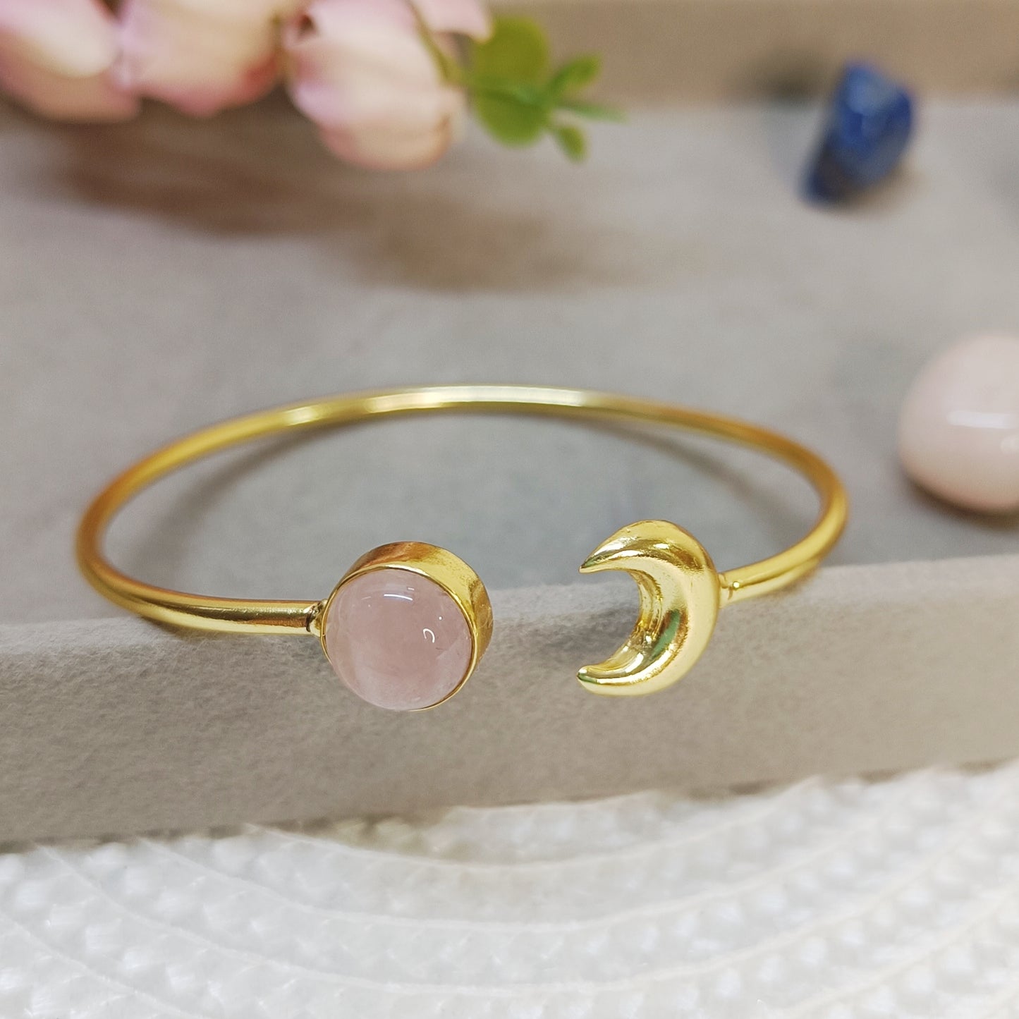 Close-up of Rose quartz cuff bangle showing brass moon charm and gold-plated finish. 