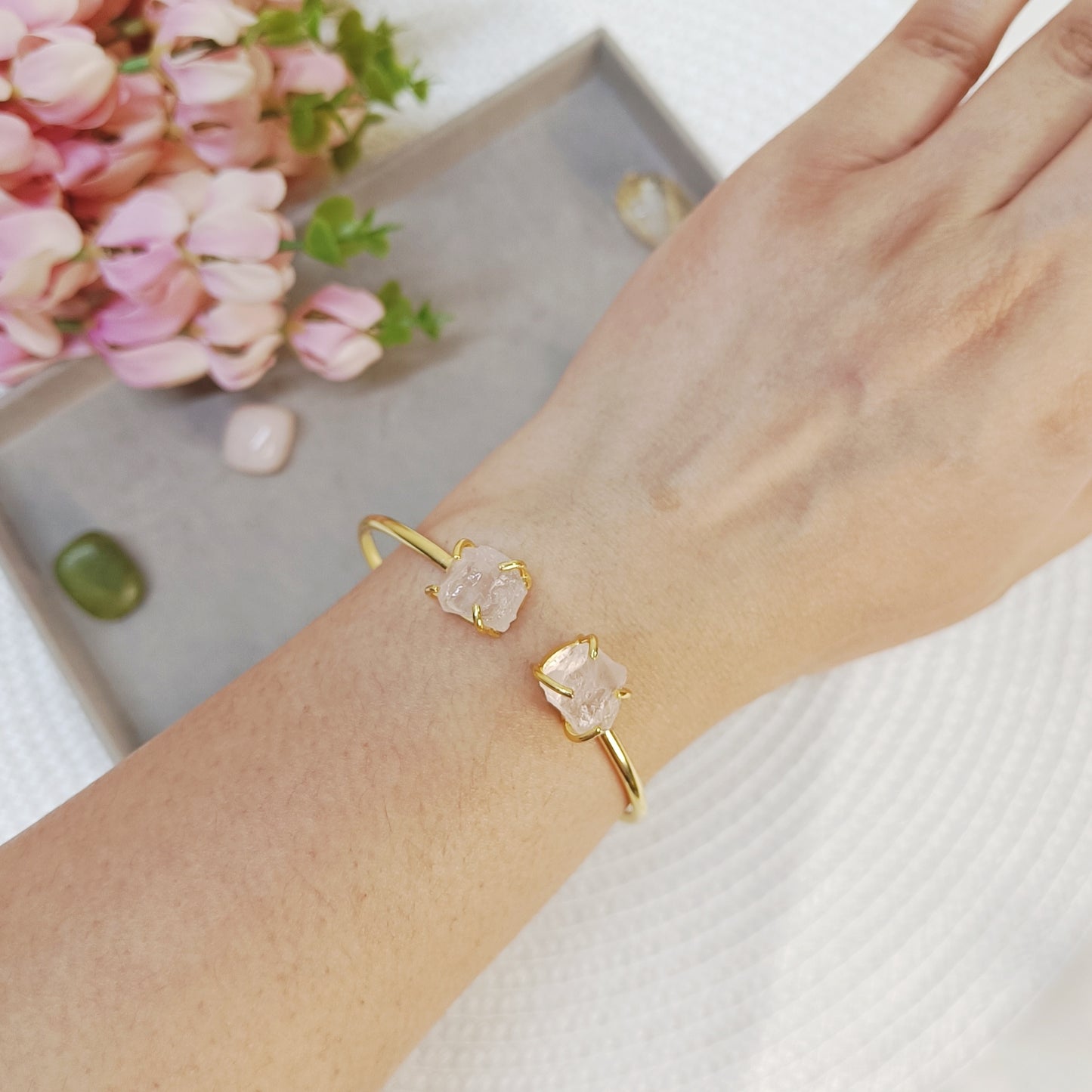 Hand wearing a baby pink stone adjustable bangle, hand wearing a rose quartz cuff bangle